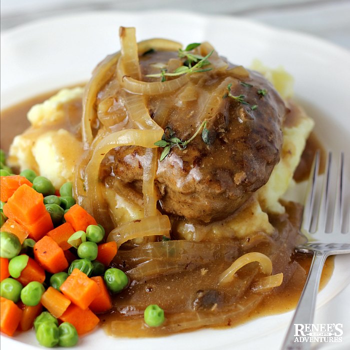 Slow Cooker Salisbury Steak over mashed potatoes with onion gravy on top on a plate