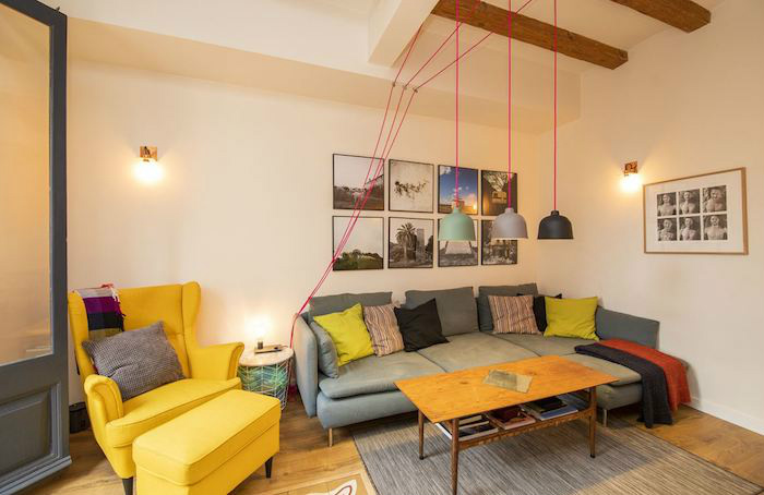 Cómo decorar un apartamento joven con poco dinero: salón con vigas y suelo de madera. Sofá y reposapiés amarillo