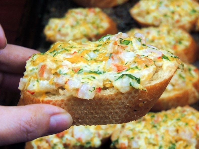 Hand holding a crostini topped with cheesy shrimp