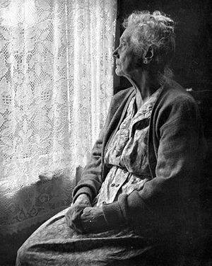 old woman looking out of window with lace curtains