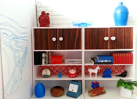 One-twelfth scale miniature retro woodgrain and white display units containing various objects in red, teal, white and black.