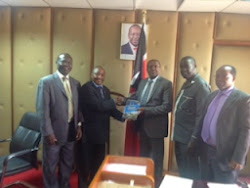 The Principal Secretary Industry Dr. Wilson Songa receives the SME Handbook from Mr. Muteti