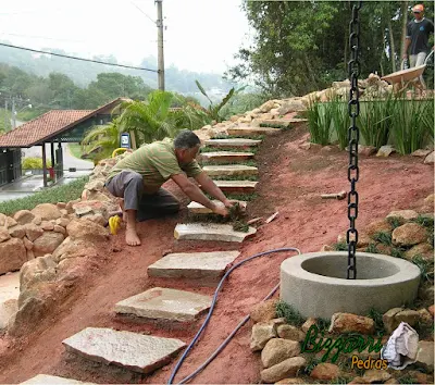 Escada de pedra cacão Goiás com tamanho entre 0,40 a 1,00 m e espessura entre 6 a 10 cm. Escada de pedra assentada com cimento, areia e  terra com junta de grama preta e com a execução do paisagismo na lateral da escada.