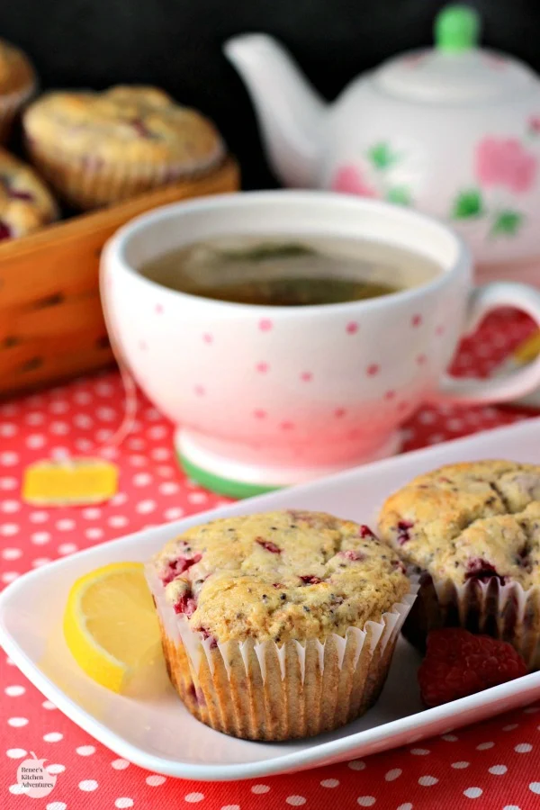 Lemon Raspberry Chia Seed Muffins by Renee's Kitchen Adventures on a white platter with a cup of hot tea in the background and a basket of muffins behind the tea cup
