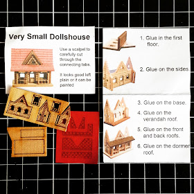 Pieces of a 'Very small dollshouse' and instruction sheet, arranged on a cutting board.
