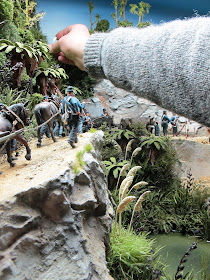 Man placing a piece of miniature toetoe grass into a diorama bush scene.