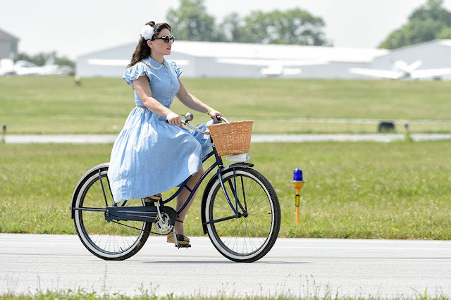 A girl in WWII period clothing riding a bike
