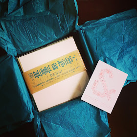 Box of dollhouse gig posters nestled in tissue paper in a postal box.