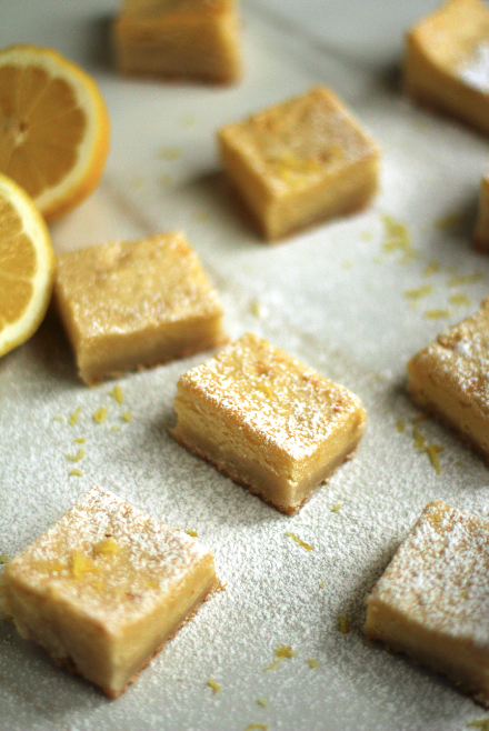 Several lemon brookies topped with powdered sugar and lemon zest next to sliced lemons.