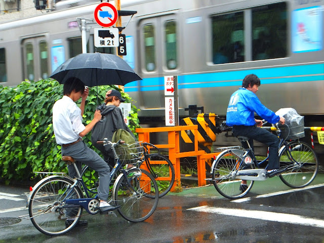 Cyclist in Tokyo wait patiently in the rain for a commuter train to pass.