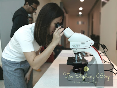A medium long hair girl in white top and grey bottom looking into the microscope in a laboratory