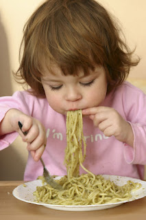 young child eating pasta with pesto sauce
