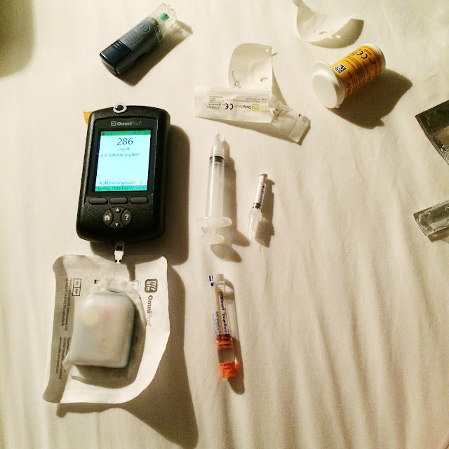 Auf dem Bett liegen Teststreifen, ein Ersatzpod und der PDM. Der PDM zeigt einen Blutzuckerwert außerhalb des Zielbereichs an.