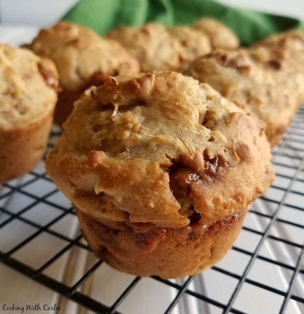 These muffins are bursting with apple flavor! They bring a healthy punch of oatmeal, sourdough, whole wheat flour and yogurt as well. Start your day off deliciously! close up of muffin on cooling rack with melty caramel showing