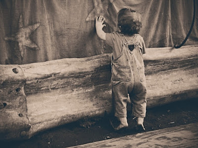 Young tot standing and holding onto a wooden structure