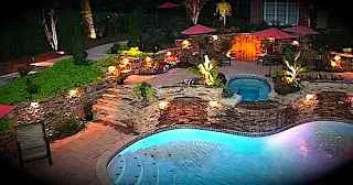 Backyard at night with swimming lit swimmimg pool.