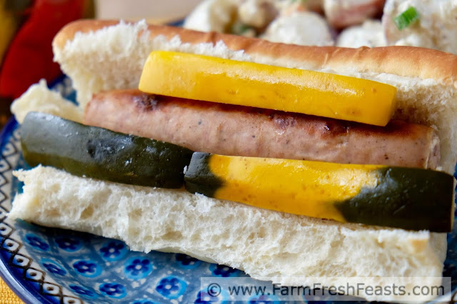 a close up photo of a bratwurst sandwich with hot and spicy zucchini pickles
