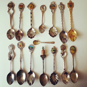 Fifteen vintage souvenir teaspoons arranged in rows on a white background