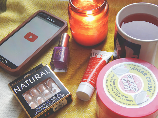 Flat lay photo with a phone, fake nails, nail polish, face mask, mug of tea, bodybutter and a candle