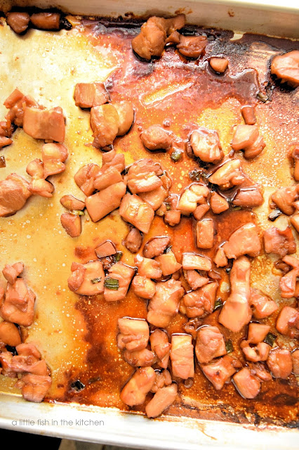Cooked teriyaki chicken pieces are on a baking dish in a pool of teriyaki sauce. 