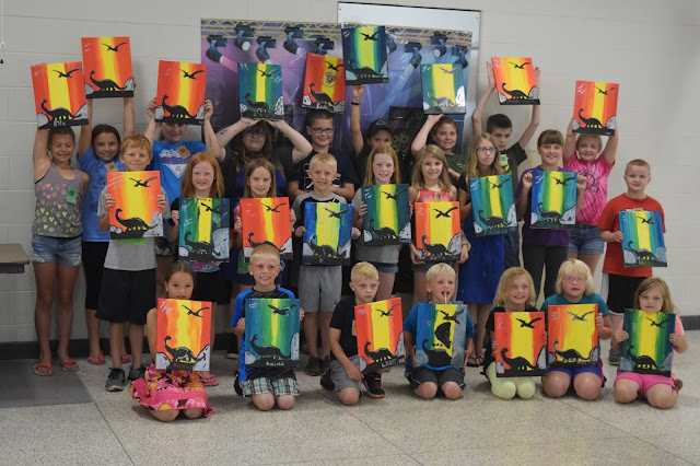 kids holding their paintings, which all feature two dinosaurs and rocks.