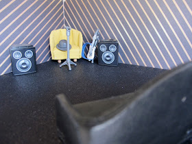 Corner of a live-music venue, with an armchair behind a mic and next to speakers. Next to the chair is a guitar.