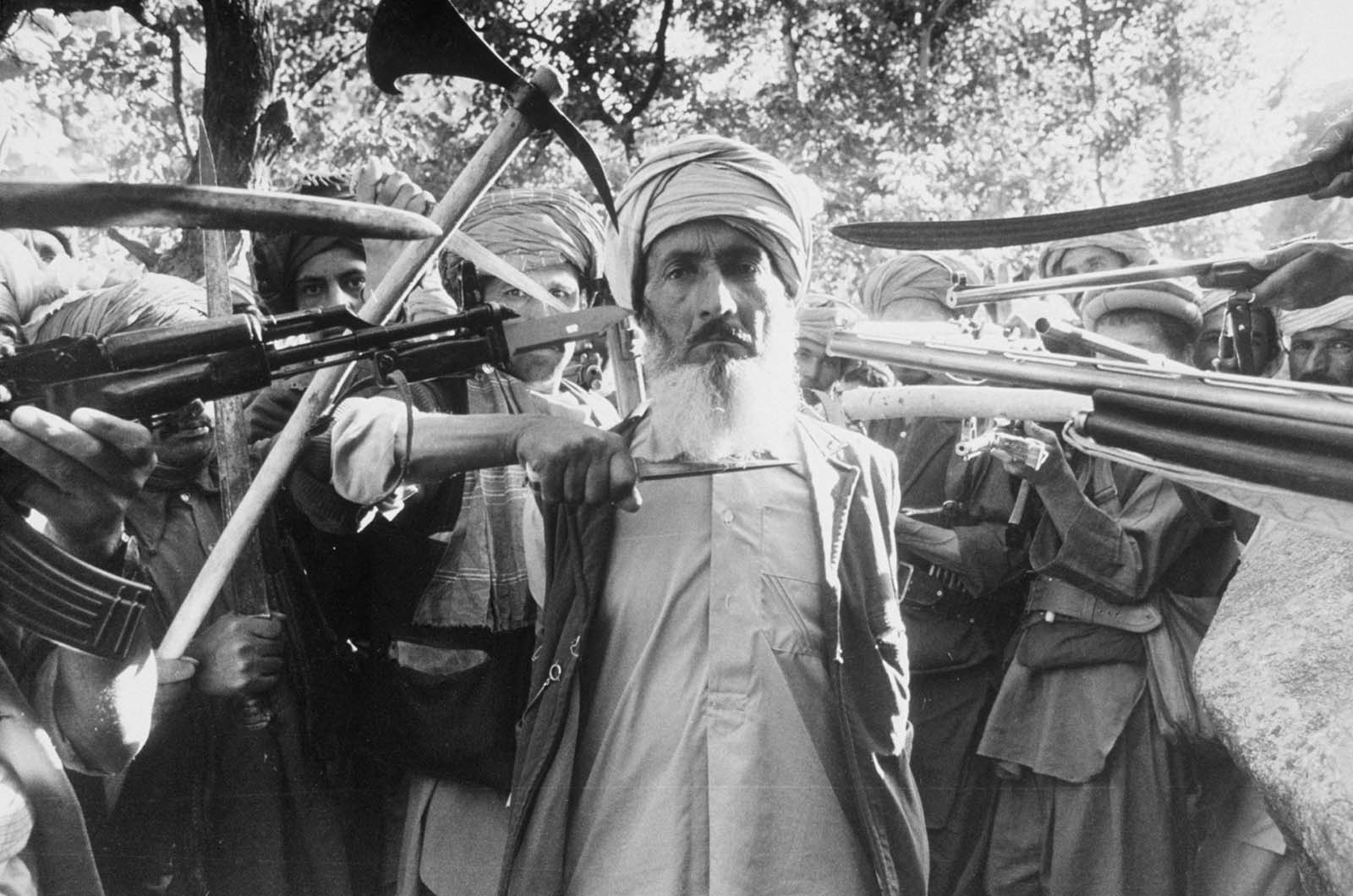Condemned by an Islamic war tribunal for denouncing nine families, a man is escorted 20 km outside Kabul for execution. 1980.