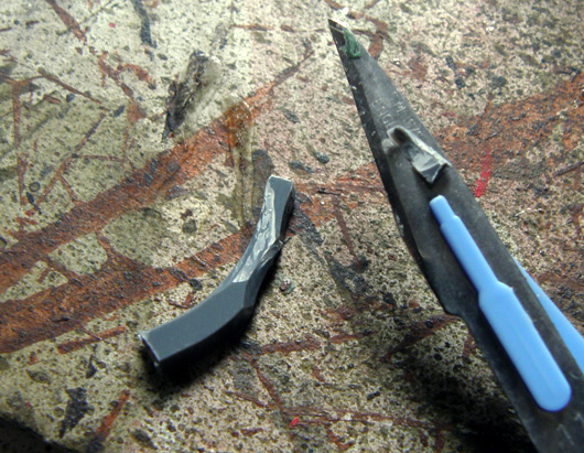 The sprue from previous photo is shown shaved from one side, with the tool used - a scalpel, seen on the right.
