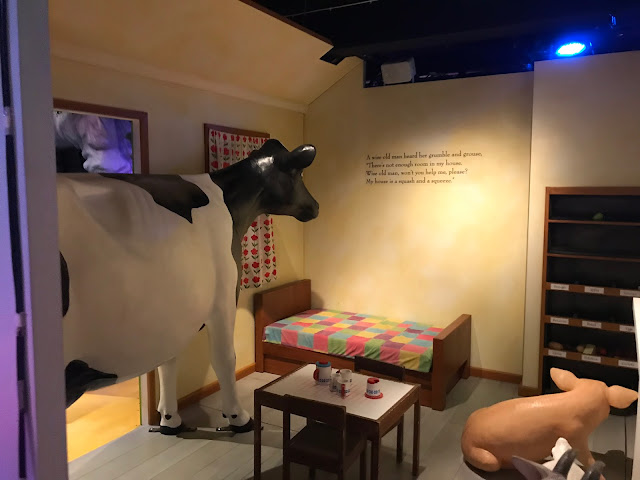 A room with a small bed and table as well as a large cow, pig and goat