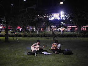 two young men sitting on the grass playing acoustic guitars at night in Zhuhai