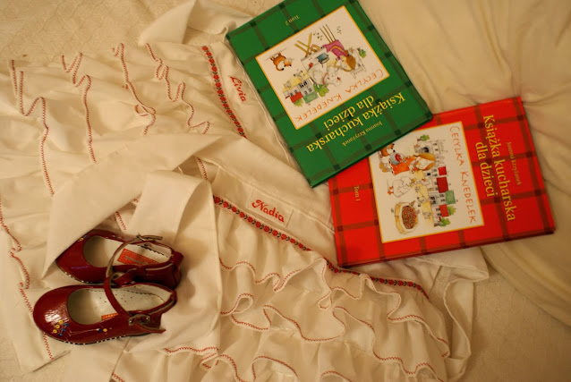 czerwone dziewczęce lakierki na białych fartuszkach z falbankami i dwie książki kucharskie dla dzieci