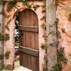 One-twelfth scale miniature door in a garden wall, slightly ajar and showing the garden behind.