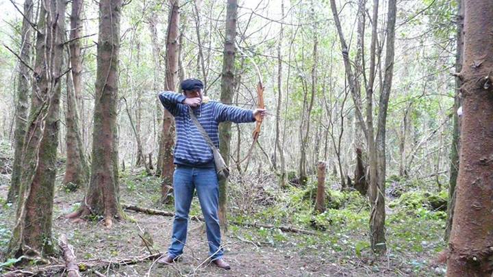 A man in a forest taking aim with a recurve bow 