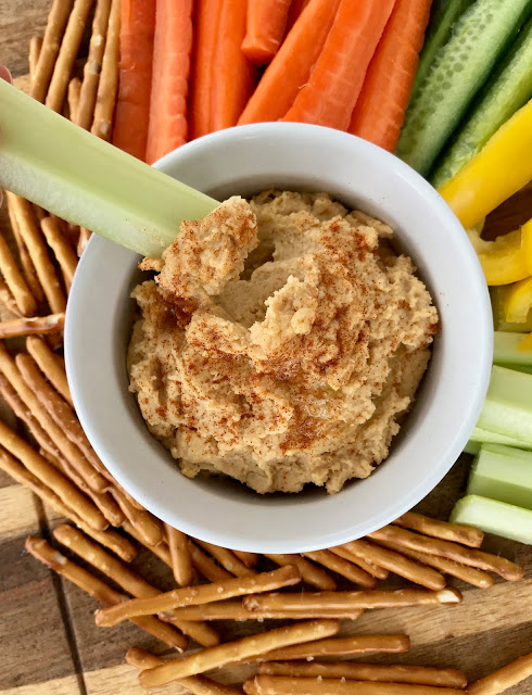 Bowl of peanut butter hummus with a celery stalk being dipped in.