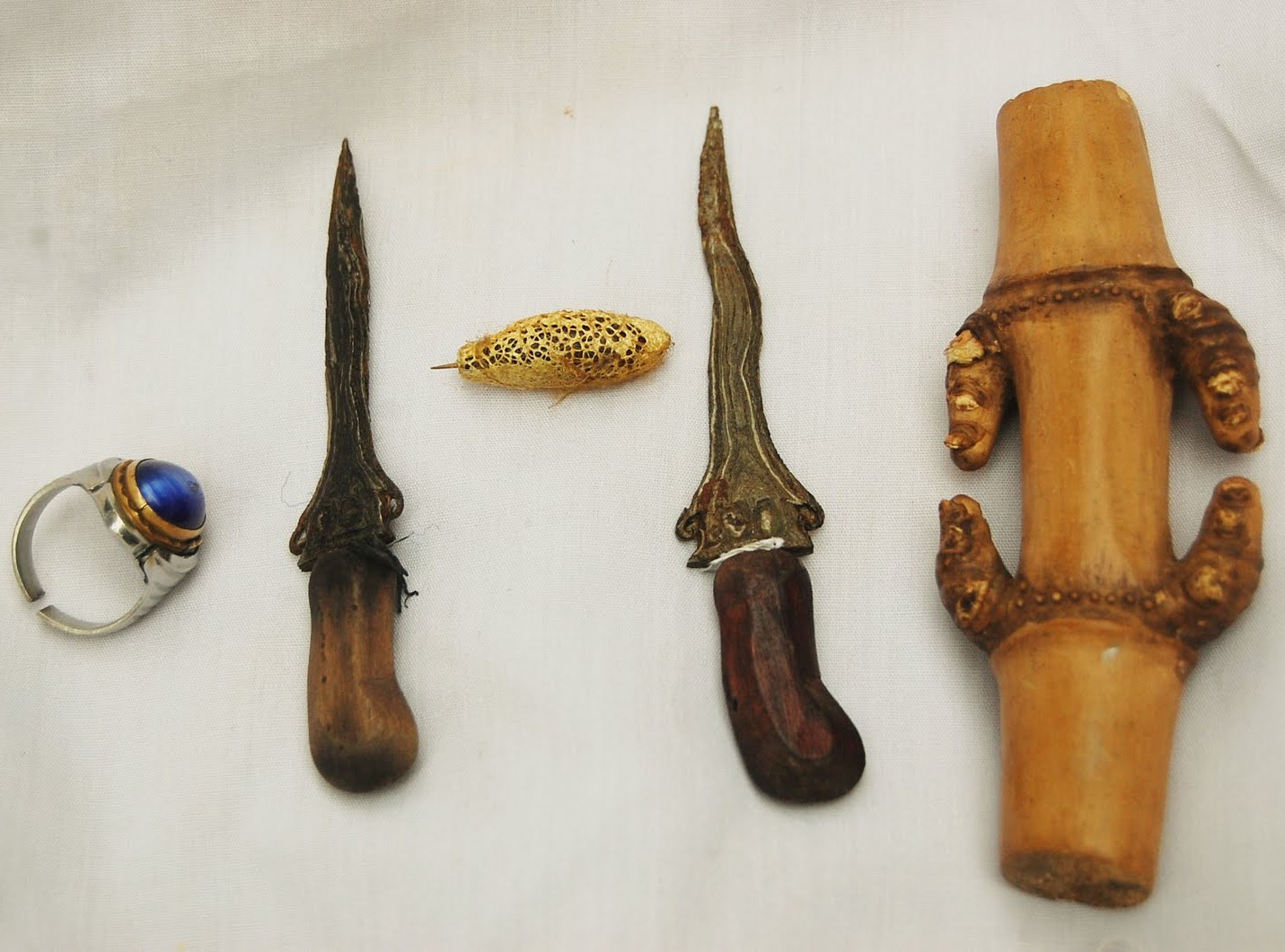  A kris, a ring, a keris, and a bamboo container are displayed on a white cloth.
