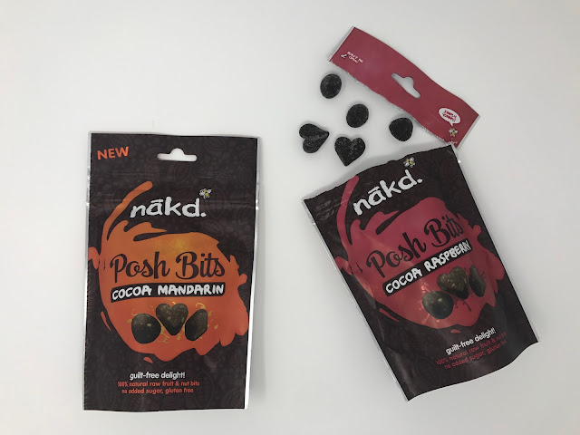 Two packets of Nakd posh bits, one is ripped open with brown bits spilling out