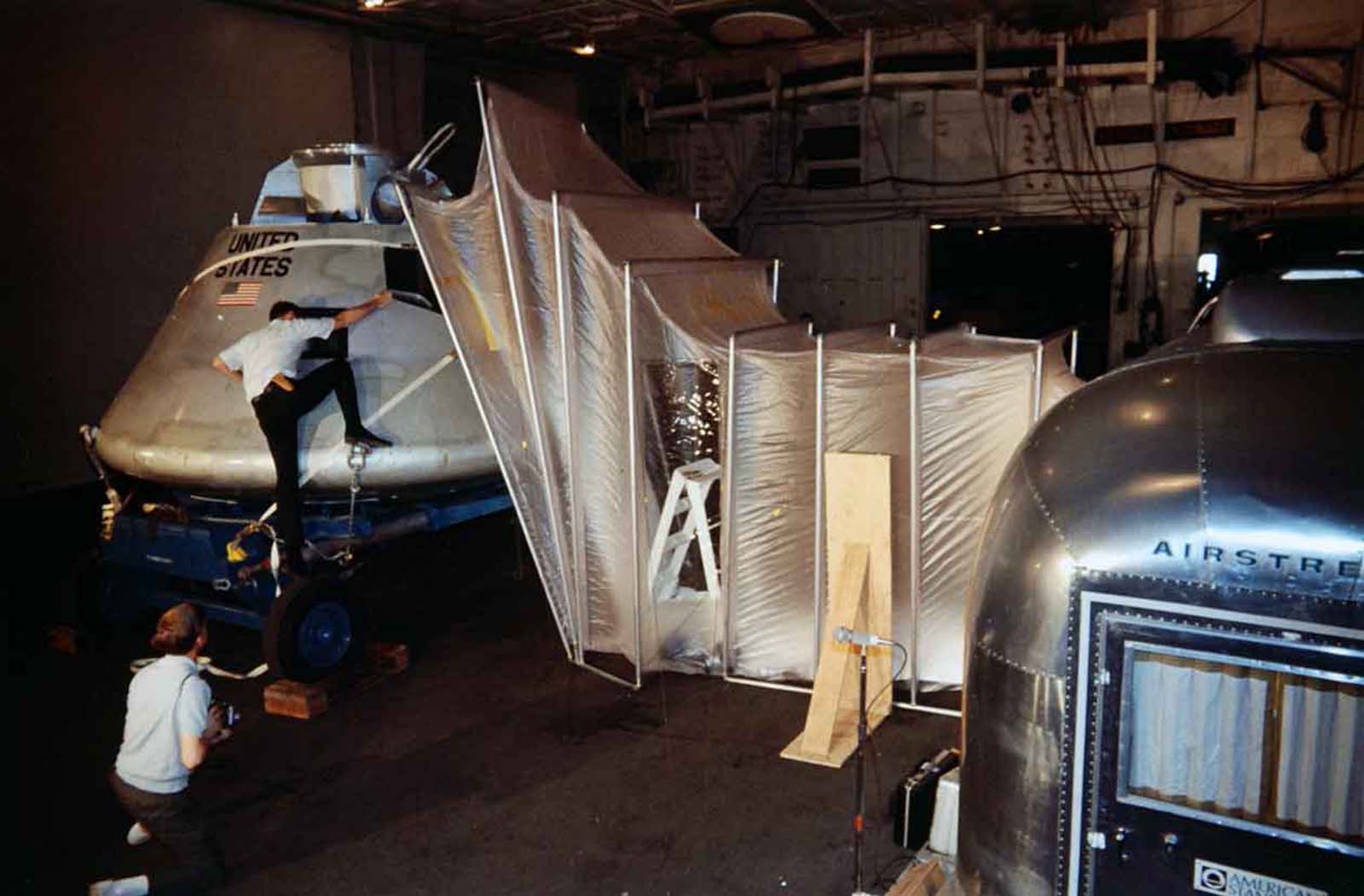 Man climbing at the Apollo Command Module inside the Mobile Quarantine Facility.