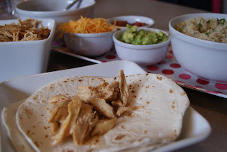 A single flour tortilla, topped with shredded chicken, along side of shredded cheese, guacamole, and shredded chicken all in bowls along side of the tortilla on a white plate.