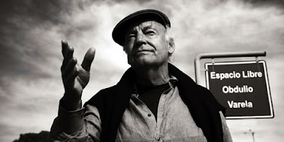 Eduardo Galeano, em preto e branco, em primeiro plano com a mão estendida, como se estivesse falando algo a alguém