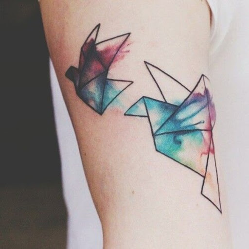 Um par de origami guindastes são acentuados com manchas de aquarela neste tatuagem conjunto representado o portador da parte superior do braço.