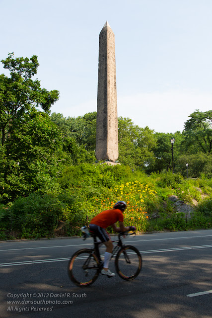 a photograph of a cyclist near the obelisk in central park