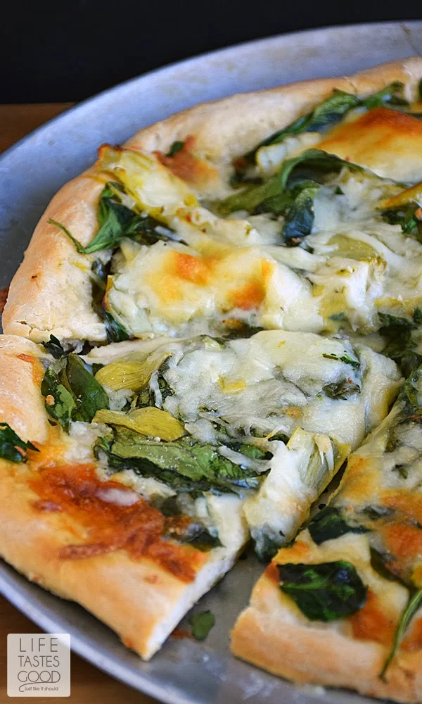 Spinach Artichoke Pizza Recipe | by Life Tastes Good is like eating one of your favorite dip recipes in pizza form! The crust is smothered in an easy-to-make, creamy white Gruyere cheese sauce and then topped with fresh spinach, marinated artichoke hearts, and even more cheese. This pizza smells so good while baking and tastes even better! #SundaySupper