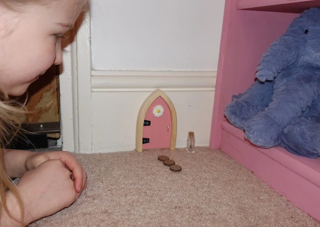 A girl on the floor peering at a pink fairy door, with stepping stones and a key from the Irish Fairy Door Company
