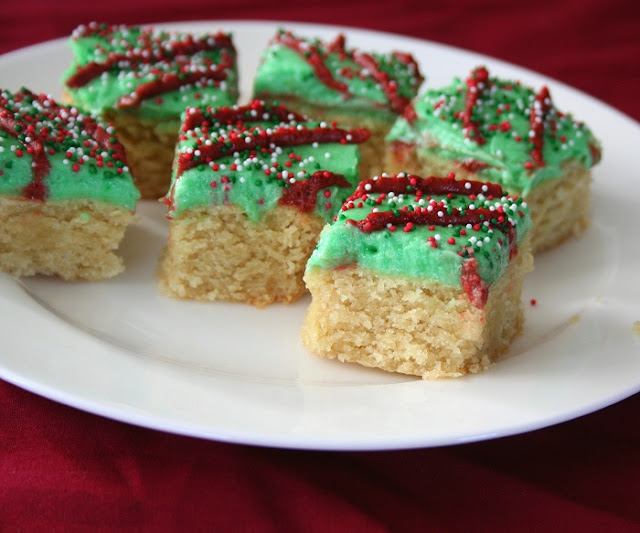 low carb and gluten free sugar cookie bars with green frosting and nonpareil sprinkles on a white plate and red tablecloth