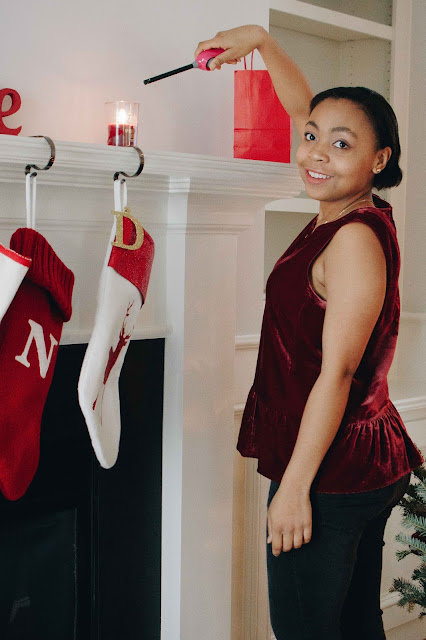 Cranberry velvet peplum top with black jeans, lighting a candle on the fireplace mantle