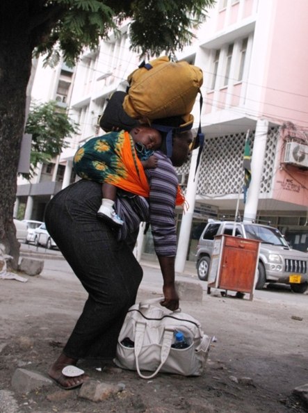 A woman struggles to pick up a bag while she balances the load she is already carrying with a baby on her back as captured along Samora Avenue in Dar es Salaam Saturday. (Photo by Mohamed Mambo)