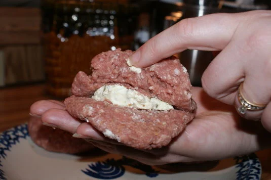 Burger patties being stuffed with cream cheese jalapeño mixture.