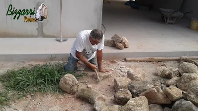 Bizzarri trabalhando, fazendo o corte das pedras moledo para fazer o revestimento de pedra na parede, com pedra moledo na cor bege com espessura de 15 a 20 cm.