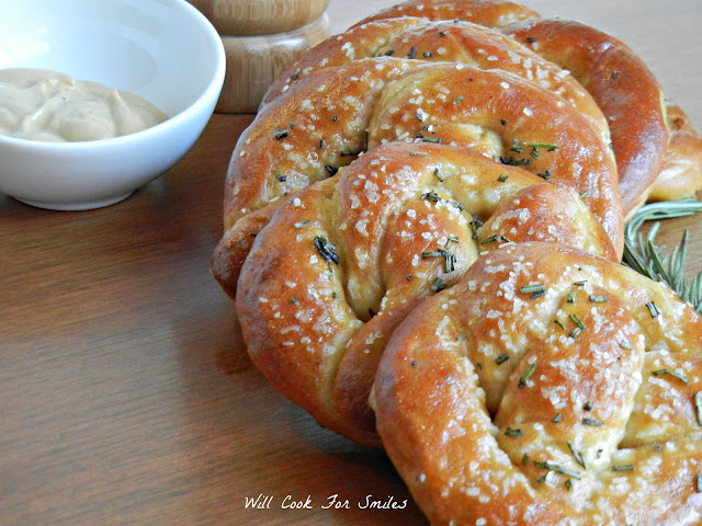 cooked pretzels lined up on a wood cutting board with a bowl of dipping sauce 