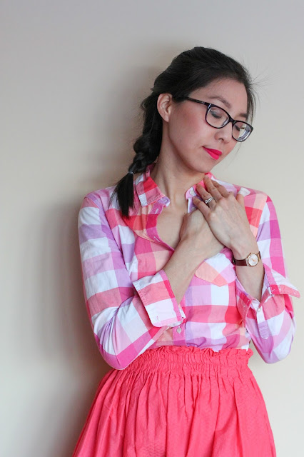 [Image of a tan skin bespectacled Asian woman wearing a plaid pink button down tucked into an elastic waist A-line coral skirt she made for herself years ago. Her arms are crossed. Her dark brown hair in a French braid. She’s got on her favorite hot pink lippie. With eyes closed she has her hands on top of each other over her heart.]